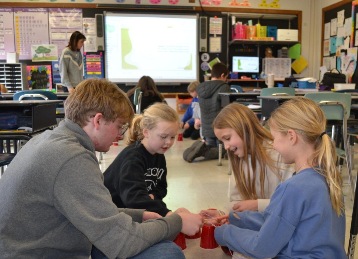 Junior Cyrus Turner stacks cups with rubber bands alongside students from Julie Lombardi’s fourth grade class. 