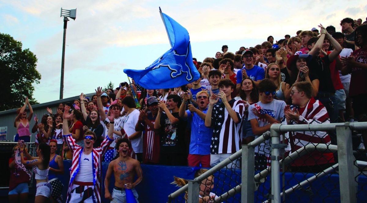 Senior Henry Elmore waves the Bexley Lion flag as student section leaders and crowd cheer loudly after a touchdown.