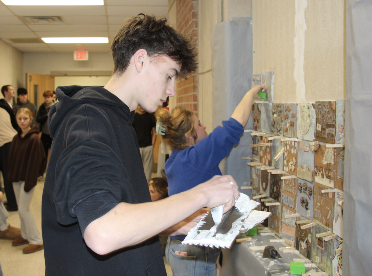 Sophomore Harrison Spring applies adhesive to the back of a tile.